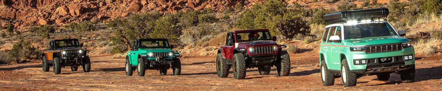 Four Jeep Brand concept vehicles being driven single file on an off-road trail in Moab, Utah during the 2024 Easter Jeep Safari. From first to last: a green 2024 Jeep Wagoneer Vacationeer Concept, a red 2024 Jeep Wrangler Lowdown Concept, a green 2024 Jeep Willys Dispatcher Concept and an orange 2024 Jeep Gladiator High Top Concept.
